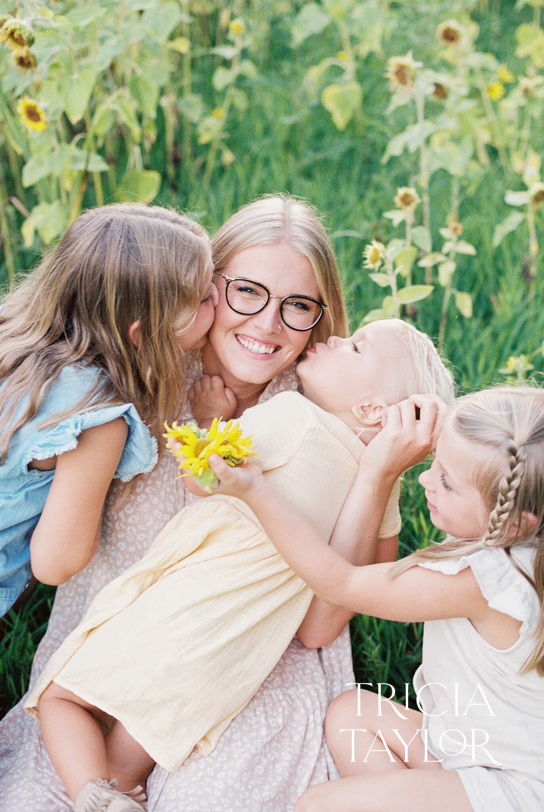 A mother sits in a sunflower field getting kissed and attacked by her three daughters Things to do in paducah