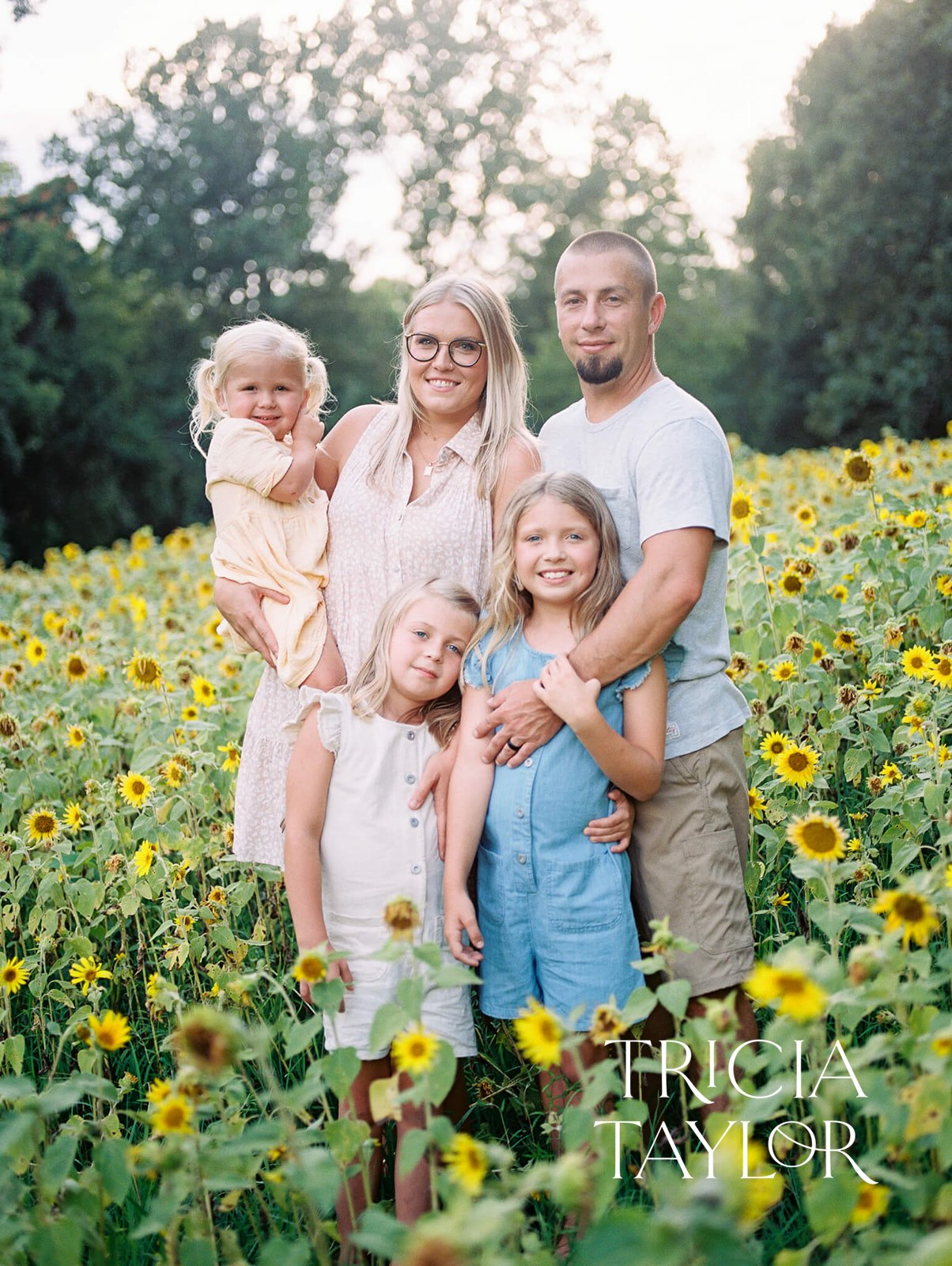 A family of five stands together in a field of sunflowers