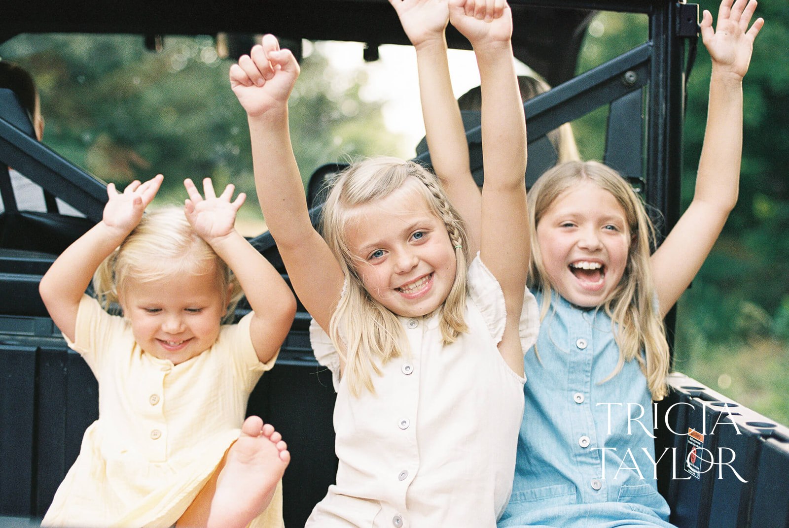Three sisters throw their hands in the air while riding in thee back of an ATV